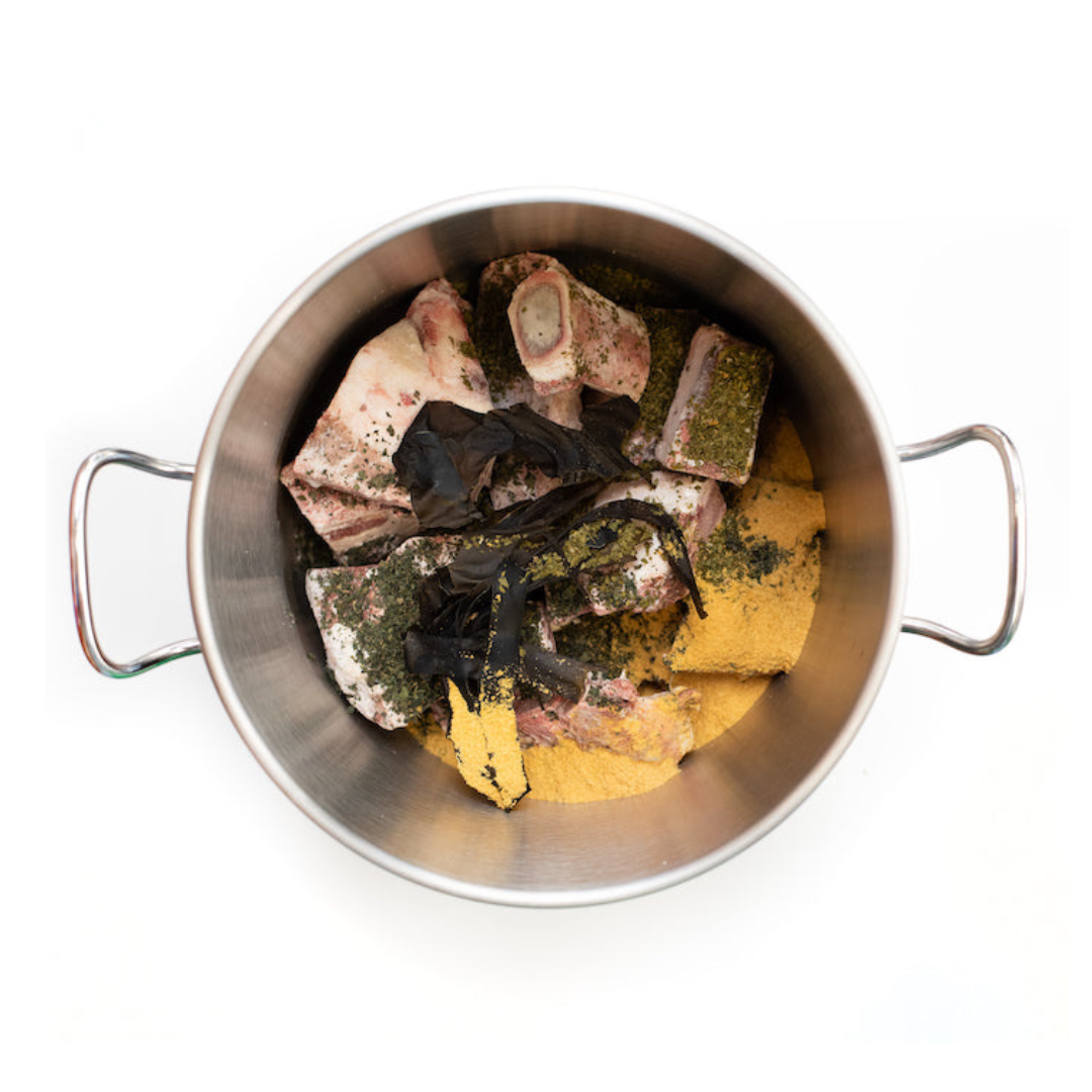 Overhead photo of a selection of freshy-cut animal bones in a large silver pan sprinkled with a variety of herbs.